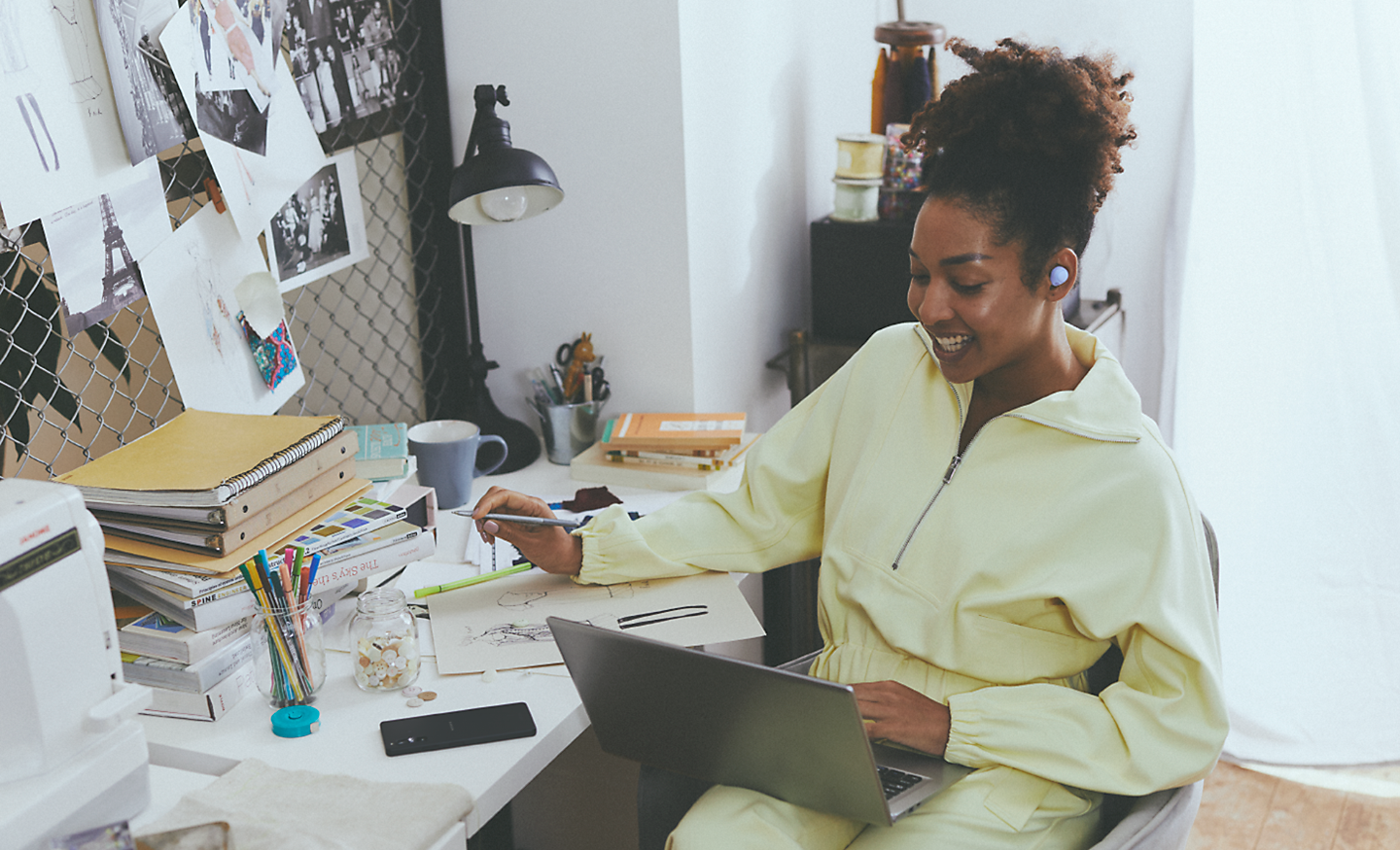 Abbildung einer Frau an einem vollen Schreibtisch, die an einem Notebook arbeitet und lavendelfarbene WF-C700N kabellose Noise Cancelling-Kopfhörer trägt