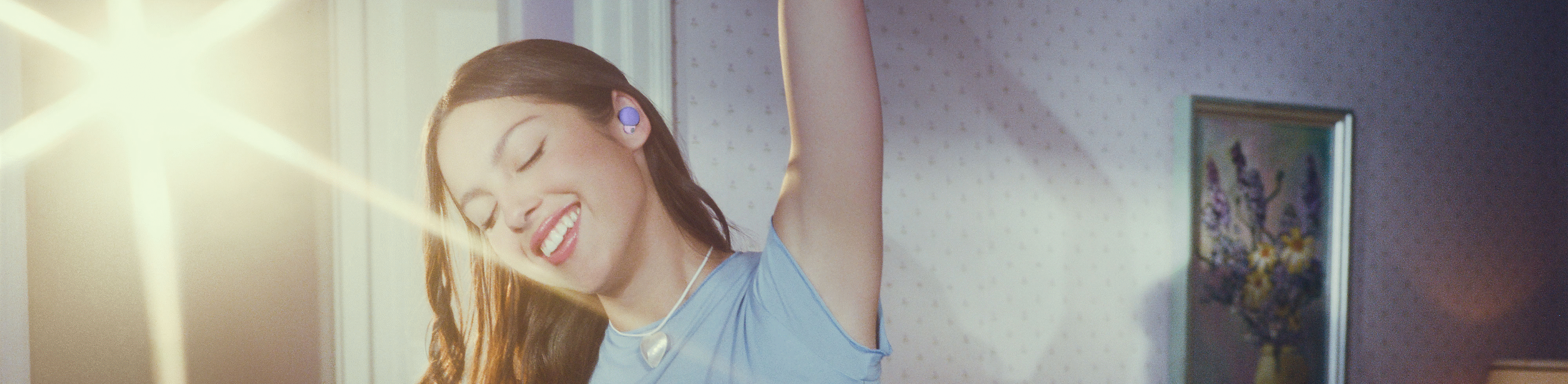 Foto Olivia mengenakan headphone LinkBuds S berwarna ungu selagi mengangkat satu lengan di atas kepala dengan cahaya terang di latar belakang