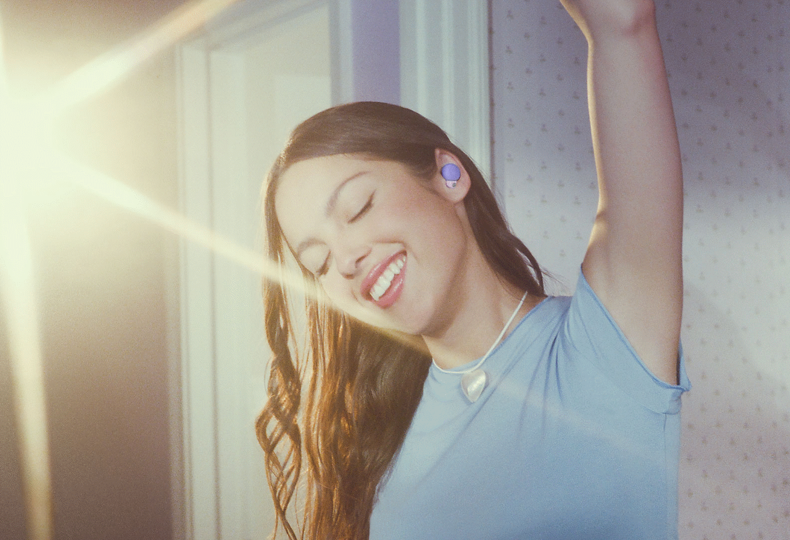 Imagen de Olivia usando audífonos LinkBuds S de color violeta y levantando un brazo sobre su cabeza con una luz brillante de fondo