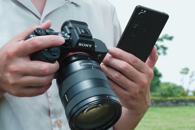 O fotografie cu o persoană care ține în mână Alpha 7 IV și un smartphone pentru a partaja fotografii sau filme imediat după ce le face