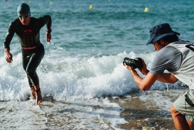 Imagen de uso de un hombre sujetando la cámara para tomar capturas a un triatleta que sale corriendo del mar