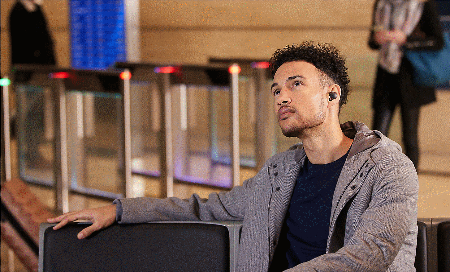A man waiting on a bench at a station, wearing WF-1000XM4 headphones