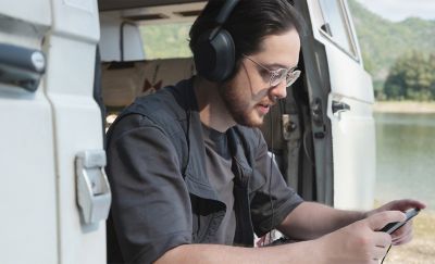 A person sitting in a camper van parked beside a lake using the Xperia 1 VI paired with wireless headphones.