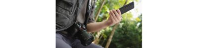 Uma pessoa com uma câmera SLR tradicional pendurada no pescoço e um Xperia 1 VI na mão.