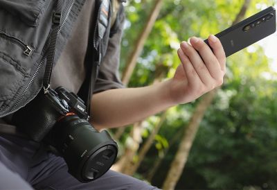 一個人脖子上掛著傳統的單眼相機，手裡拿著 Xperia 1 VI。