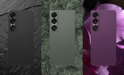 3 phones seen from the back showing the lenses in a grid.  To the left the slate black phone placed on an image of a slate tile background, in the centre the moss green on an image of moss background, to the right, the orchid phone behind an image of an orchid flower background