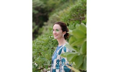 Человек в фокусе, улыбающийся в камеру, на фоне размытого изображения и полностью сфокусированного изображения листа на переднем плане, снятого на Xperia.