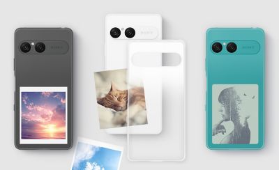 На задней панели видны чёрный, белый и бирюзовый телефоны, на которых хорошо видны фотографии и другие памятные вещи. Между белым телефоном и крышкой вставлена ​​фотография.