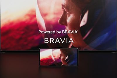 Logo Powered by BRAVIA i BRAVIA nad małym telefonem przed dużym ekranem wyświetlającym ten sam obraz