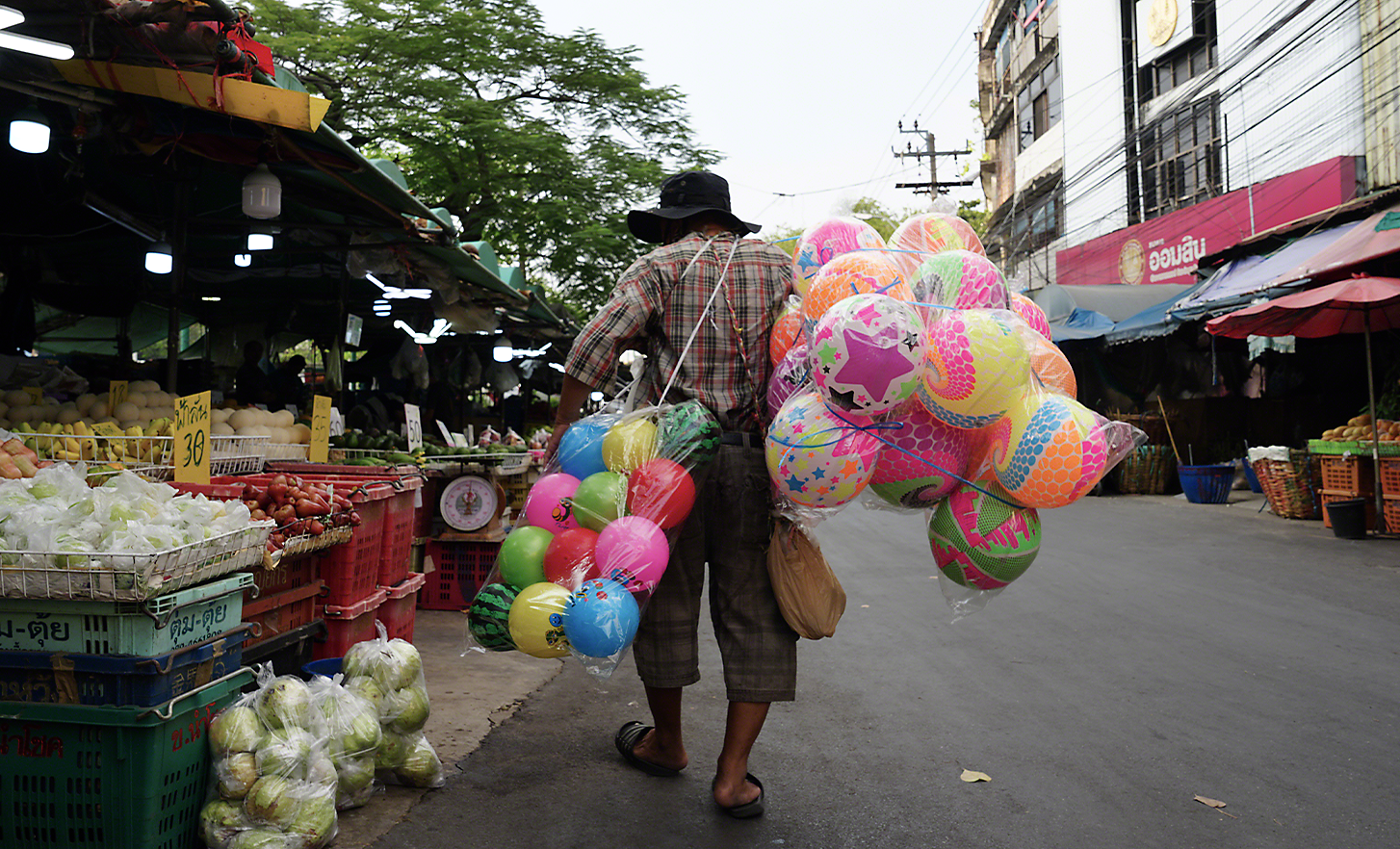 Pouličný predavač nesúci veľké tašky s výrazne farebnými plastovými loptičkami