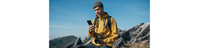 Uma pessoa em uma paisagem acidentada – ele tem uma câmera Sony Alpha pendurada no pescoço e está olhando para seu Xperia 1 V