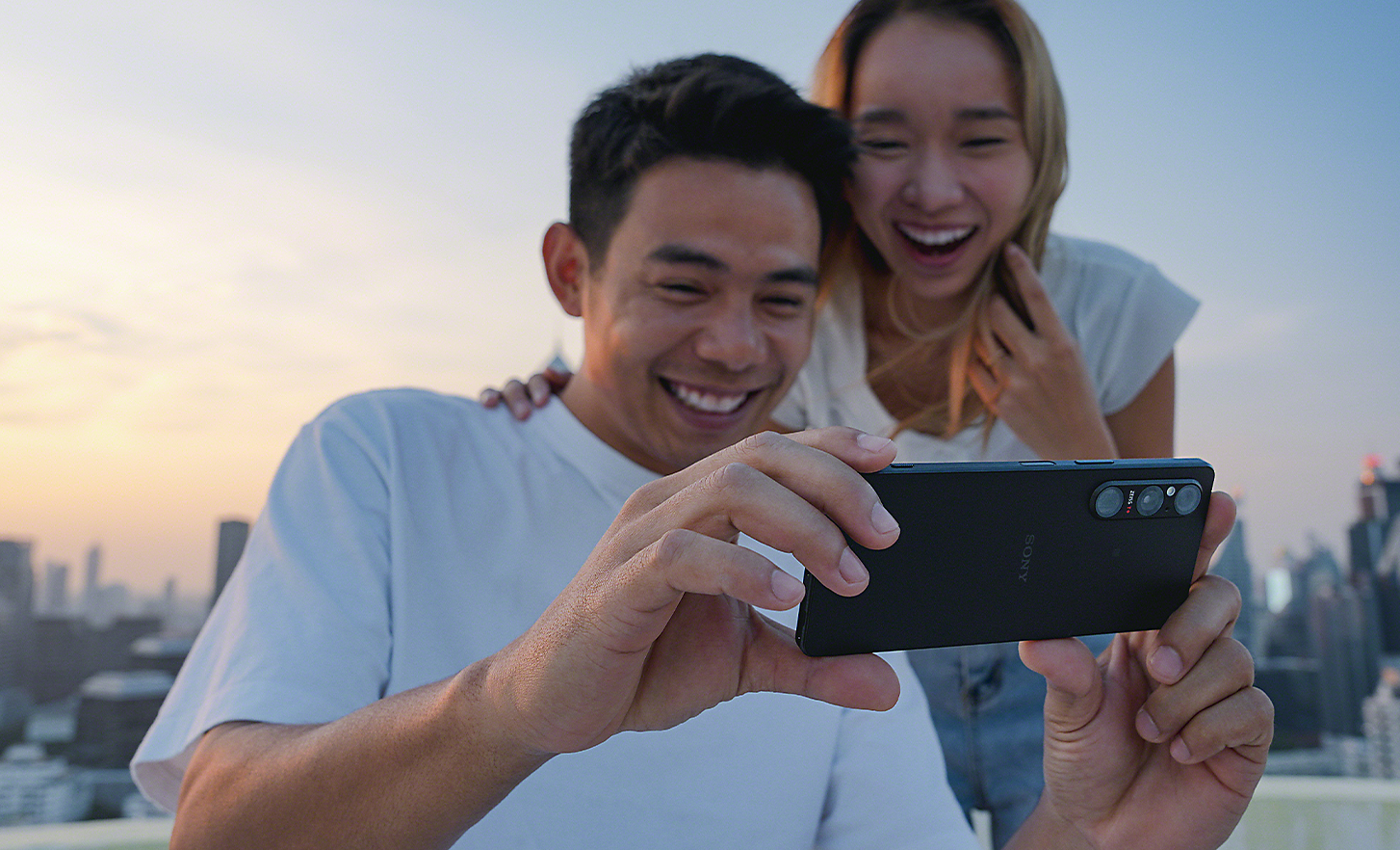 Dvaja mladí ľudia, ktorí si vonku užívajú sledovanie obsahu cez smartfón Xperia 1 V