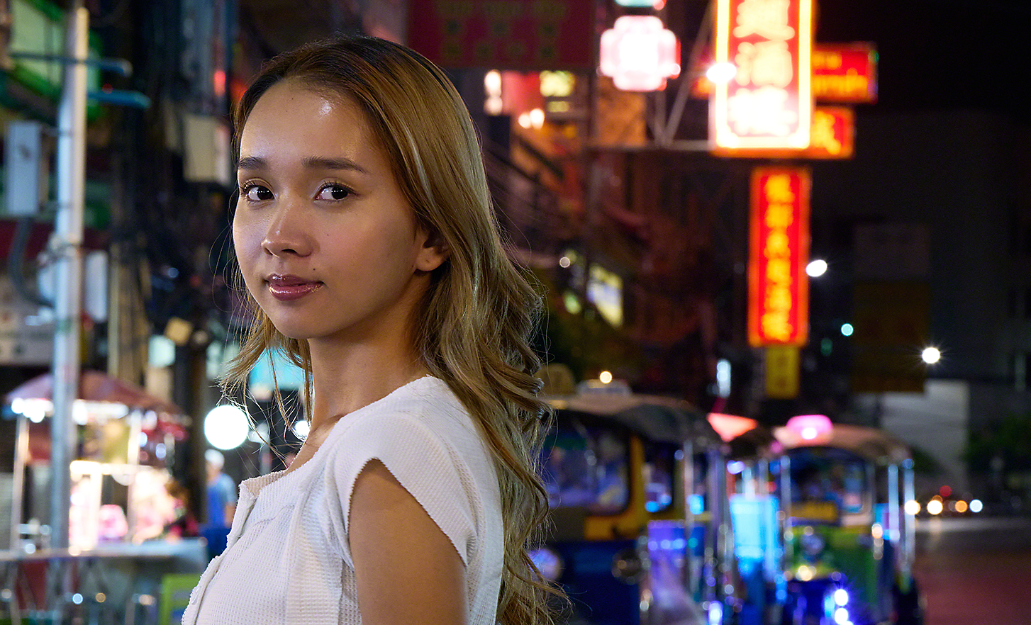 Portretopname van een jonge vrouw 's avonds in een drukke straat in de stad
