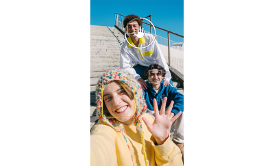 Ảnh selfie của ba người bạn đang ngồi trên các bậc cấp–một người đang giơ bàn tay lên camera và Giao diện người dùng Chụp bằng tay hiện lên