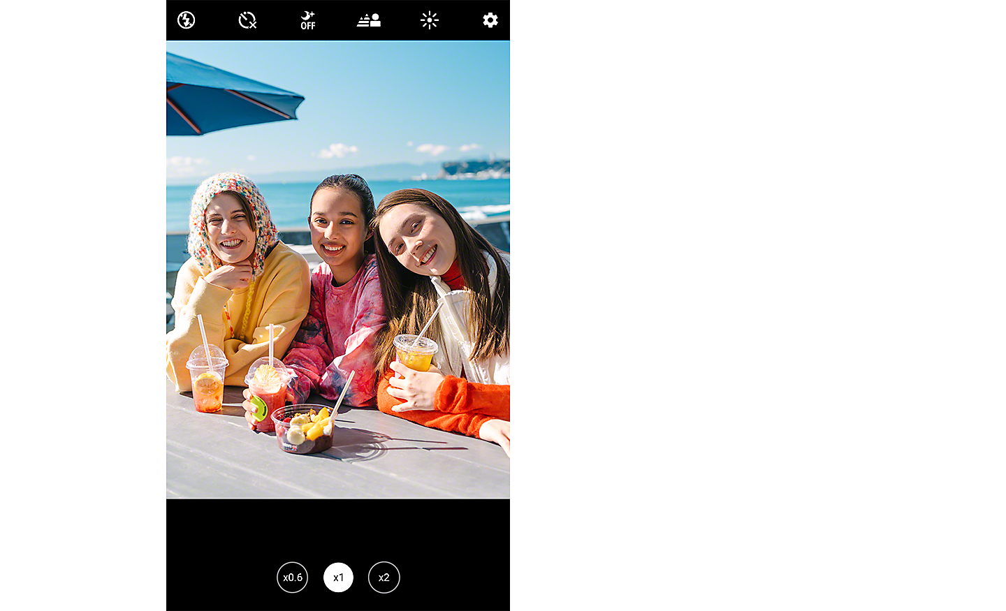 Screenshot showing an image of three young women smiling at the camera, seated at a table overlooking the sea