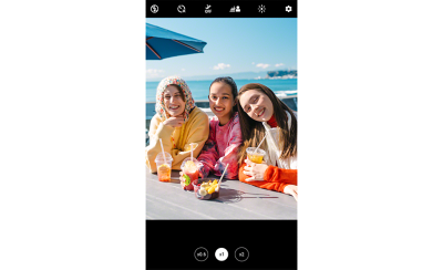 Screenshot showing an image of three young women smiling at the camera, seated at a table overlooking the sea