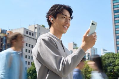 Una persona con unos auriculares puestos y un smartphone Xperia 10 VIII en una zona exterior concurrida.