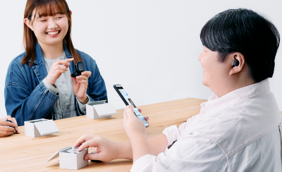 Hai người khiếm thị đang mở hộp và sử dụng tai nghe Sony LinkBuds Open trong lúc mỉm cười và trò chuyện tại bàn