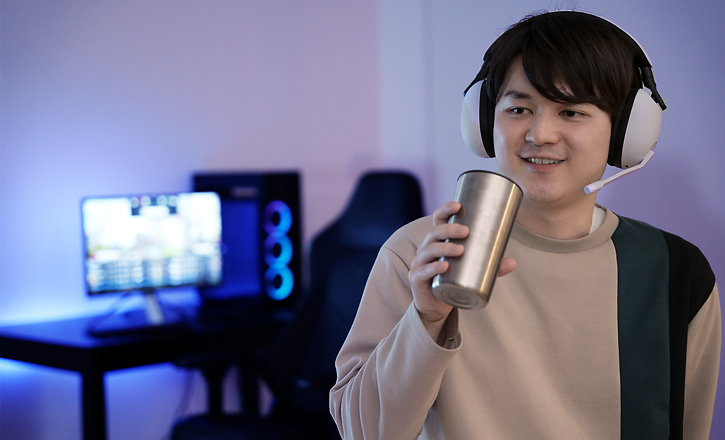 Image of a man drinking from a metal cup whilst wearing an INZONE H9 gaming headset with a PC in the background