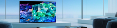 BRAVIA A95K on platform in living room with table and books in foreground and image of colourful blue, purple and green glass and crystals on screen
