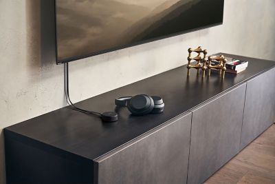 תמונה של זוג שחור של אוזניות Sony WH-CH720 המונחות על יחידת טלוויזיה מתחת לטלוויזיה מותקנת