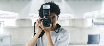 Fotografia muža držiaceho pred sebou fotoaparát s bleskom s panorámou mesta v pozadí