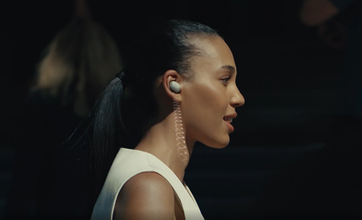 한 여성이 흰색 조끼를 입고 오른쪽 귀에 화이트 이어버드를 착용하고 있습니다. 이어버드 이미지에 아래쪽을 향한 흰색 코일 선이 추가되었습니다.