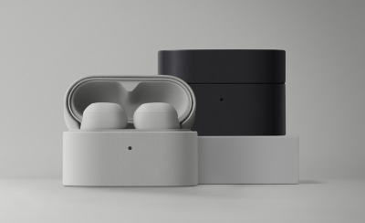 Two pairs of wireless earbuds in open charging cases, one light gray and the other dark gray, on a minimalistic gray background.