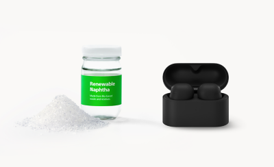 쌓여 있는 흰색 크리스털과 "Renewable Naphtha, Made from Bio-based waste and residues"라고 적혀 있는 유리병 옆에 놓인 블랙 타원형 이어버드 케이스.