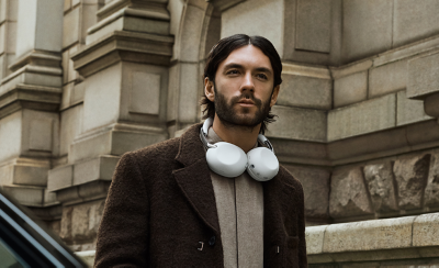 A person wearing a pair of white 1000X THE COLLEXION headphones around their neck against a building exterior