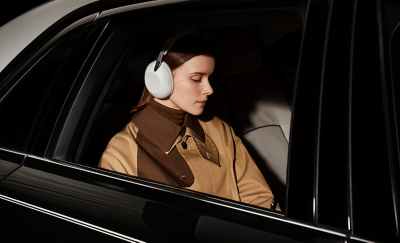 A person wearing a pair of white 1000X THE COLLEXION headphones sitting in a car with the windows rolled down