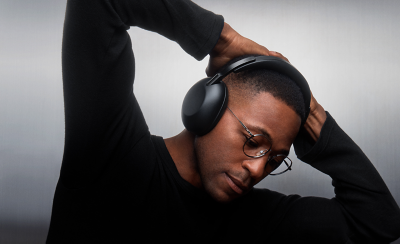 A person in a black shirt with their hands on the back of their head, wearing a pair of black 1000X THE COLLEXION headphones