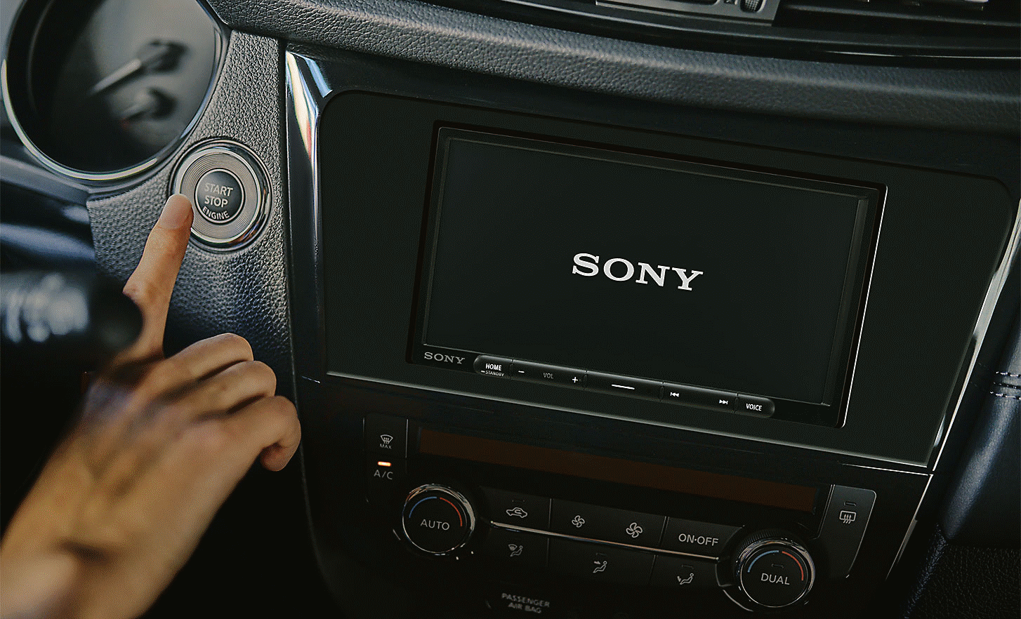 Slika uređaja XAV-AX4050 na nadzornoj ploči s logotipom Sony na zaslonu i osobom koja pritišće gumb za pokretanje automobila