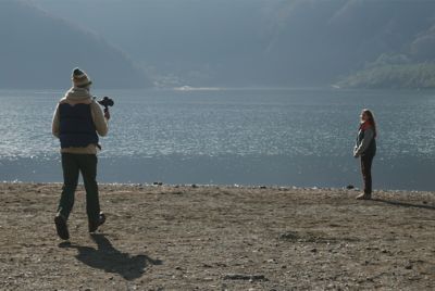 Image of a man holding a camera, shooting a woman on a beach