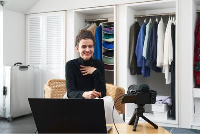 A women live streaming, in front of a laptop computer and a camera on a tripod