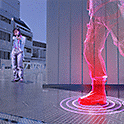 A person holding a plastic gun in a computer game world aiming at a 3D model with rings around the foot for sound