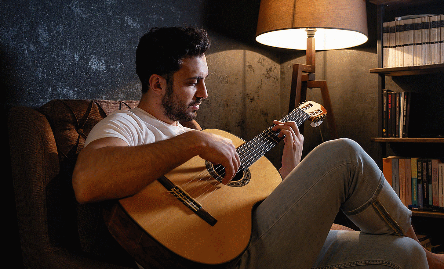Image of a person playing guitar in an arm chair