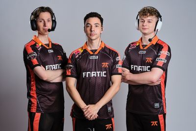 Three gamers wearing shirts with the Fnatic logo on the front. Two are wearing over ear headsets with mics, one is wearing in-ear wired headphones.