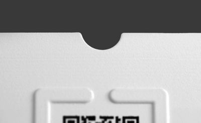 A close up of the top portion of a QR code printed on paper with a raised tactile border around it. At the top of the paper a small semi-circle is cut out.