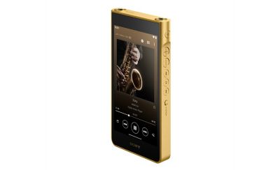 Photograph showing a gold-coloured Sony WM1ZM3 Walkman angled on a white background. The front touchscreen displays a media player interface with album art of hands playing a saxophone. Circular control buttons and headphone jacks line the metallic gold edge.