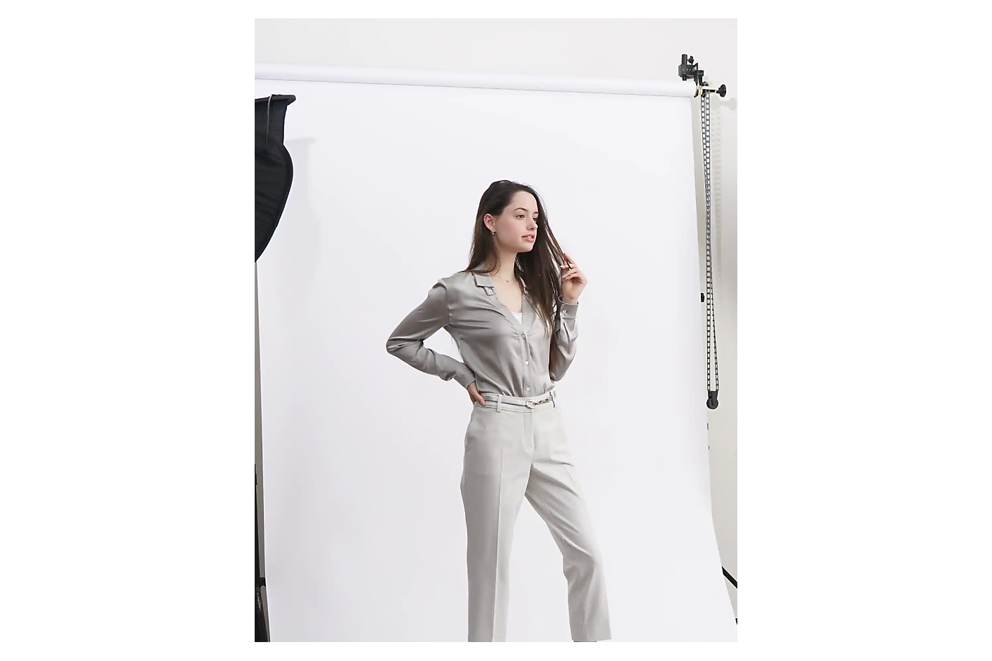 A woman in a light-grey outfit poses in front of a white backdrop in a photo studio.