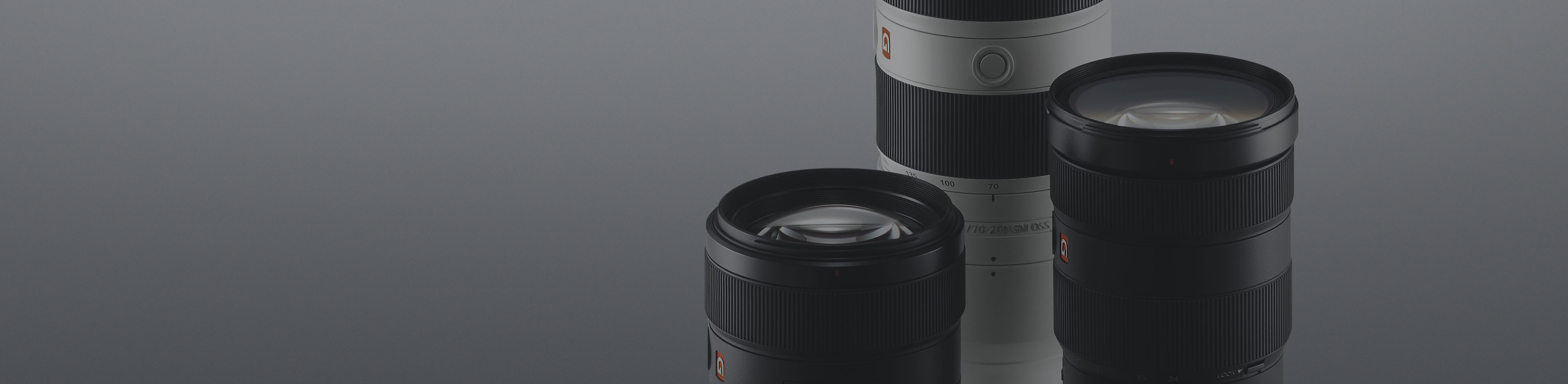 Drei schwarz-weiße α-Objektive von Sony vor einem grauen Hintergrund