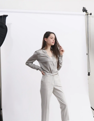 Femme en tenue gris clair posant devant un fond blanc dans un studio photo.