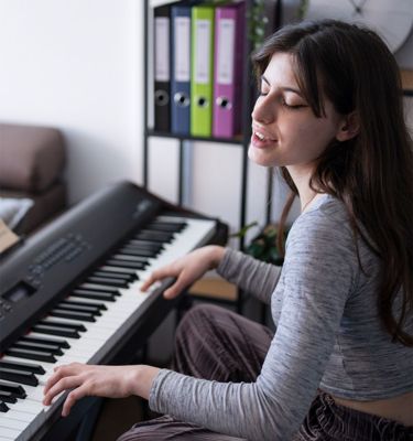 Image 101: Image of a woman sitting in her lounge playing an electric keyboard and singing