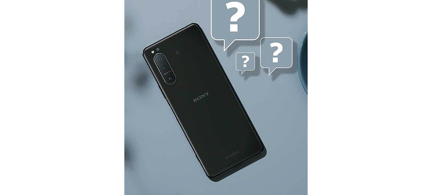 Tył czarnego smartfonu przechylony na szarym tle oraz znajdujące się obok symbole znaku zapytania w dymkach.