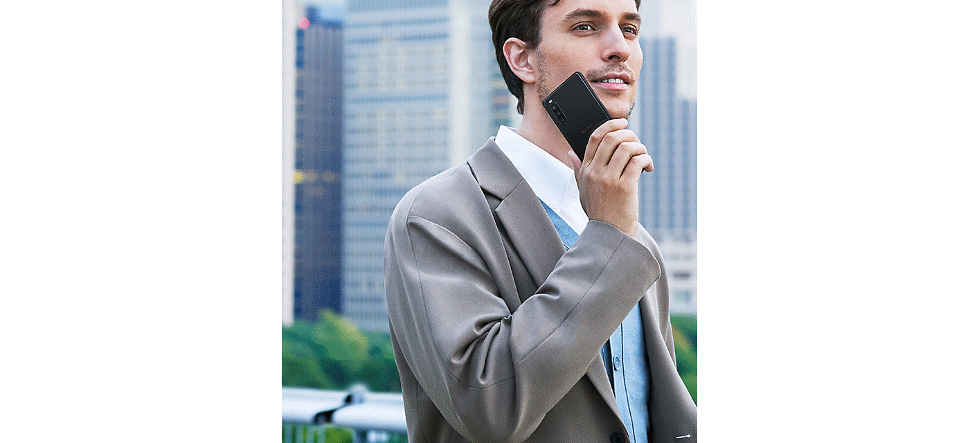 A man in a grey suit holds a black smartphone up to his cheek