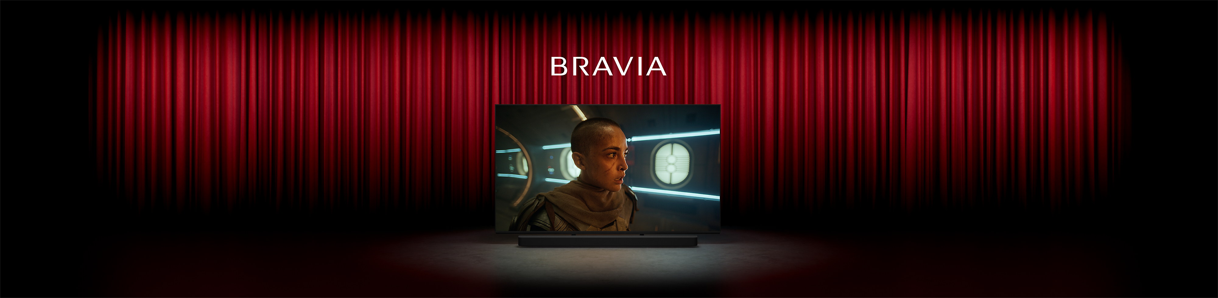 תמונה של קולנוע עם וילונות אדומים ובמה מרכזית שבה טלוויזיה של Sony, עם צילום מסך של אדם בסרט מדע בדיוני, המילה BRAVIA למעלה ומקרן קול של Sony למטה