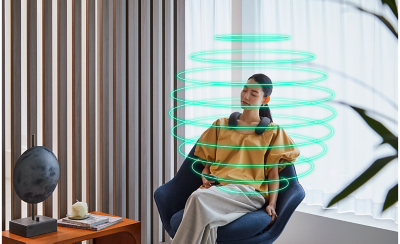 Person sitting in a chair wearing BRAVIA Theatre U with blinds to left and window behind and a green sphere encircling her showing 360 Reality Audio