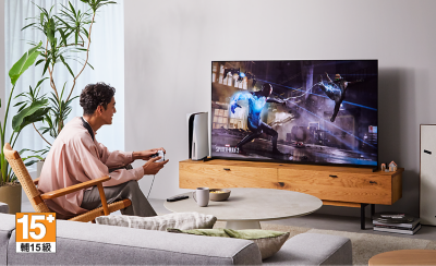 Persona sentada en una silla en una sala de estar usando BRAVIA Theatre U, mientras juega en un televisor de pantalla grande con una imagen de una escena urbana de Spider-Man 2 y el logo de 15+ abajo a la izquierda