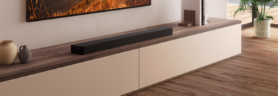 BRAVIA Theatre Bar 8 soundbar on wooden plinth with books to right and wall-mounted TV above showing road and sunburnt grass